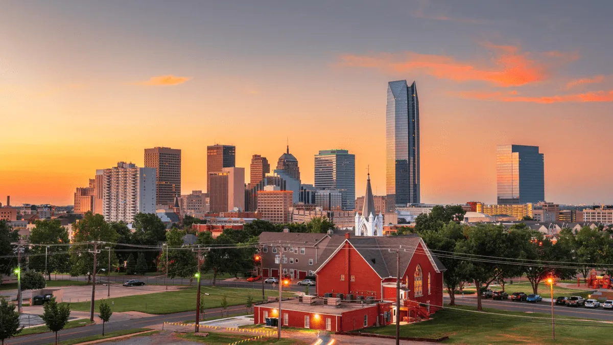 Oklahoma City skyline featuring the Devon Energy Center tower, Scissortail Park, and Chesapeake Energy Arena at sunset